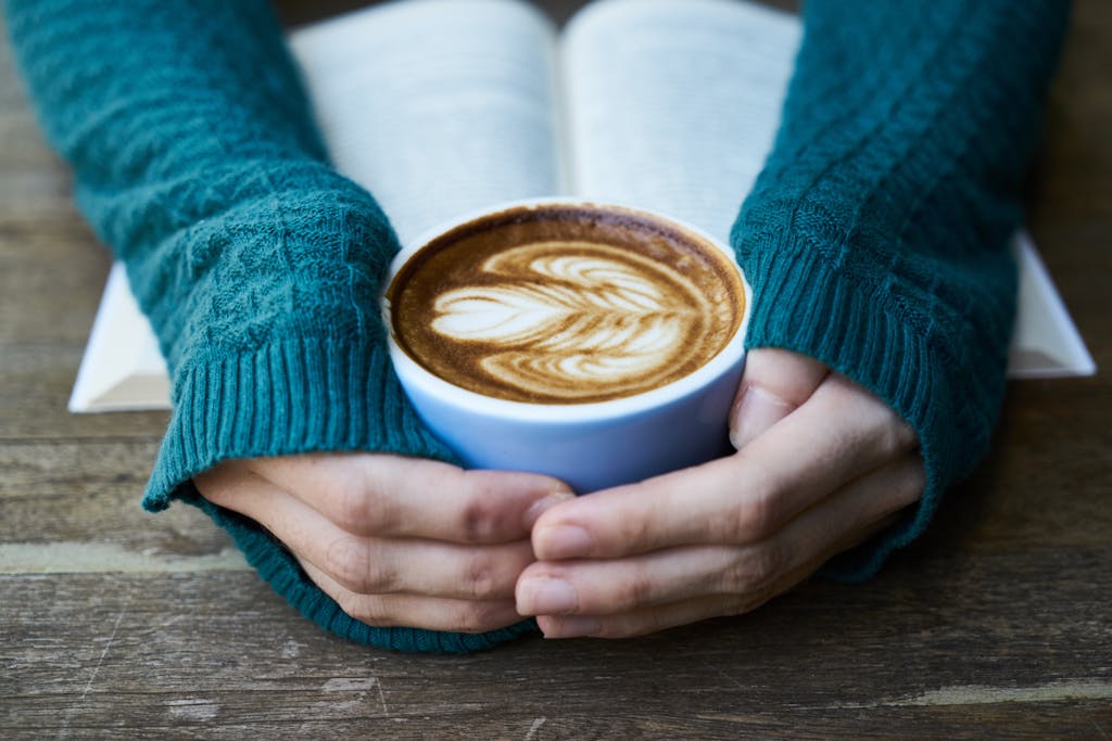 Selective Focus Photography of Cafe Latte in Cup Near Book on Table