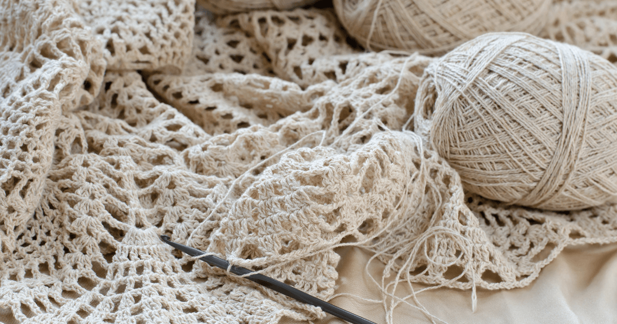 Cream-colored crocheted lace with balls of beige yarn and a crochet hook on a soft surface.