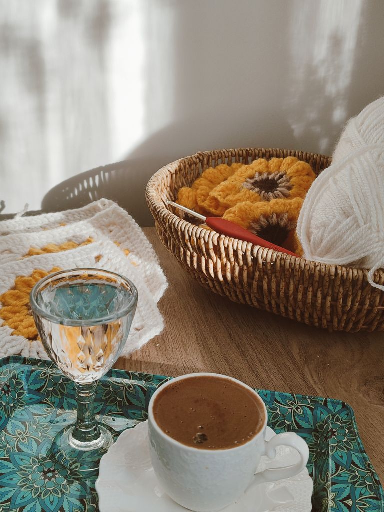 Warm sunlight over crochet basket, coffee cup, and water glass on a wooden table.