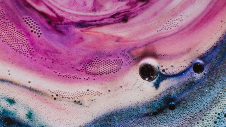 Close-up of vibrant pink, purple, and blue soap foam with scattered bubbles and circular patterns in an abstract design.