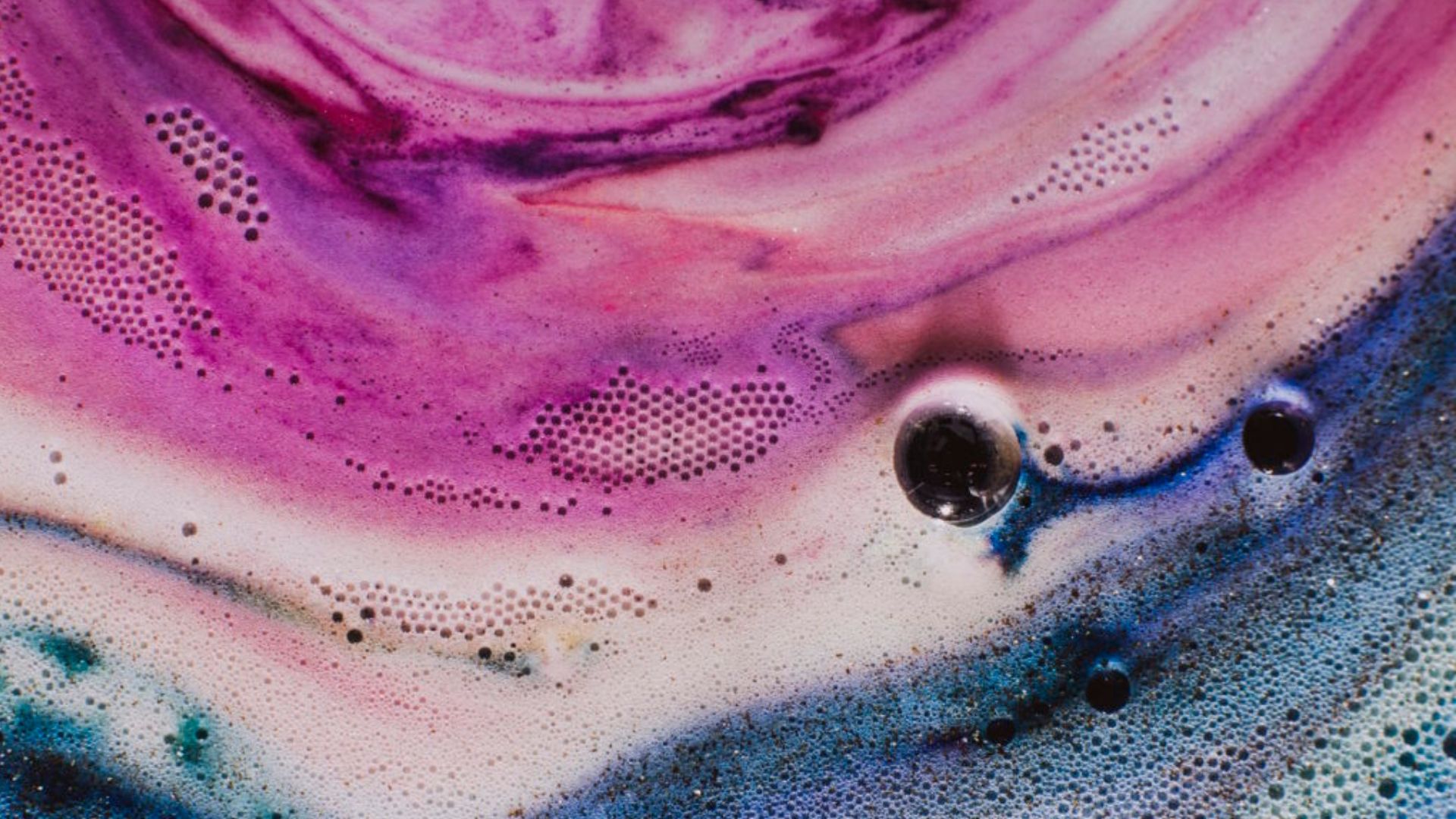 Close-up of vibrant pink, purple, and blue soap foam with scattered bubbles and circular patterns in an abstract design.