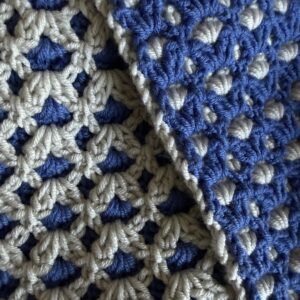 Close-up of blue and white crocheted fabric showing a granny-square motif with interlocking stitches.