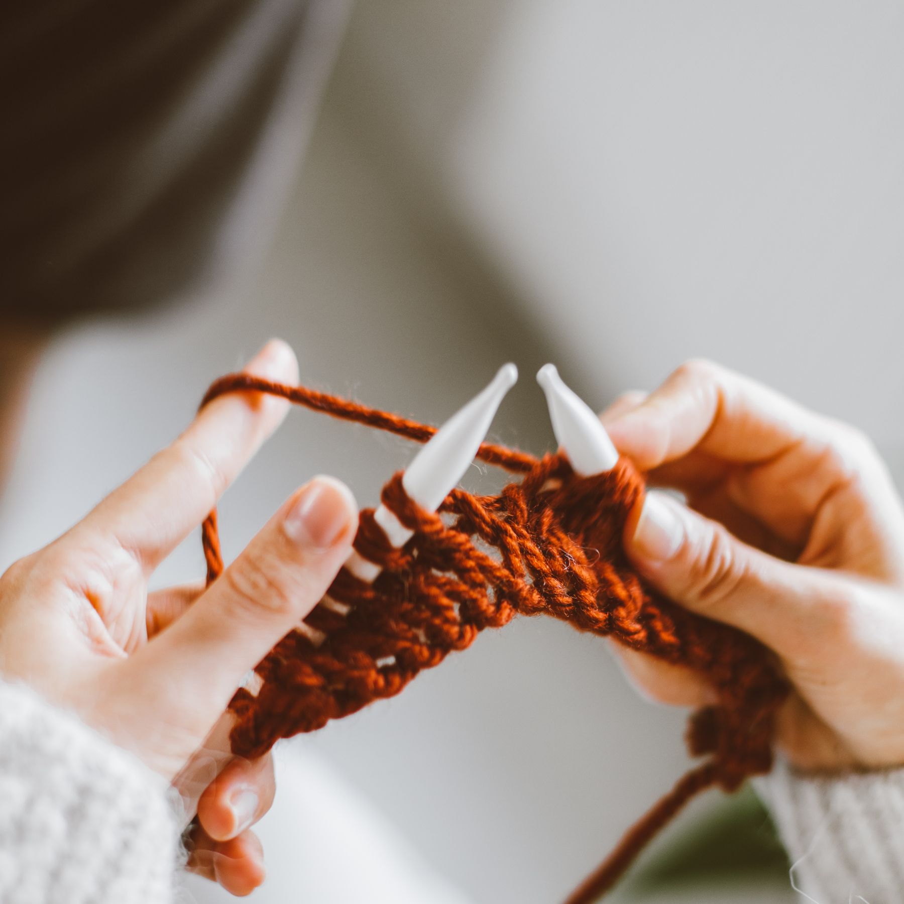 Close-up of hands knitting with orange yarn and white knitting needles.